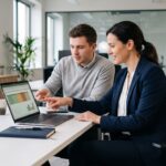 Gerente de vendas e analista financeiro apontam para uma planilha de comissão de vendas no notebook, em um escritório moderno